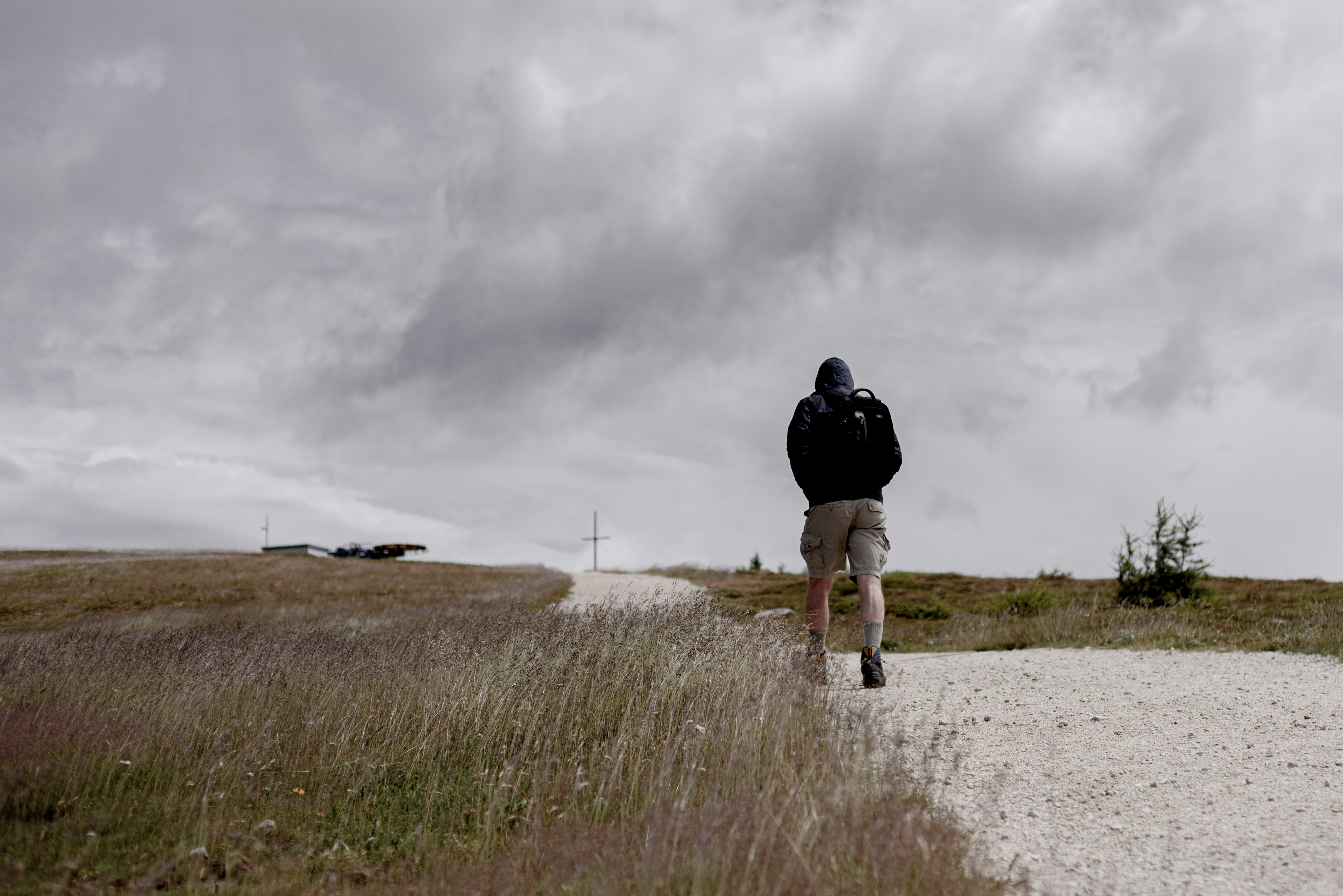 person in black jacket and black pants walking on brown field under gray cloudy sky during